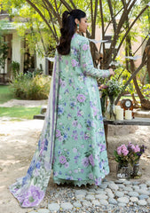 Woman in a floral dress standing outdoors with greenery and a table in the background